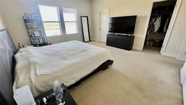 bedroom with light carpet, a closet, a walk in closet, and baseboards