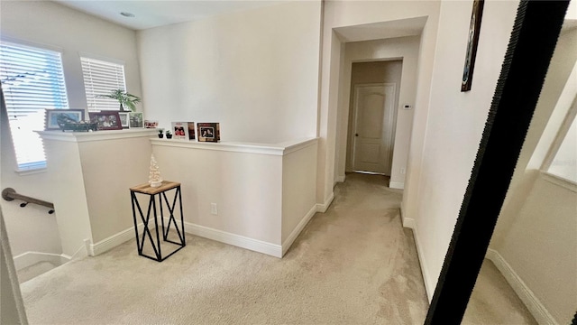 hall with an upstairs landing, light colored carpet, and baseboards