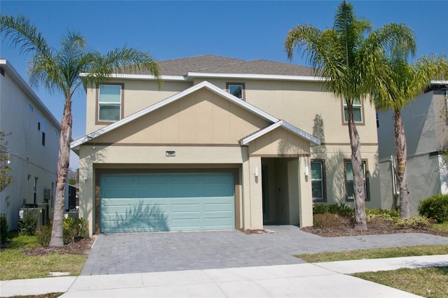 traditional-style home with a shingled roof, central air condition unit, decorative driveway, and stucco siding