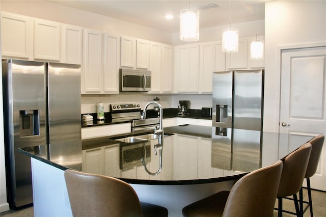 kitchen featuring a breakfast bar area, a kitchen island with sink, a sink, appliances with stainless steel finishes, and white cabinetry