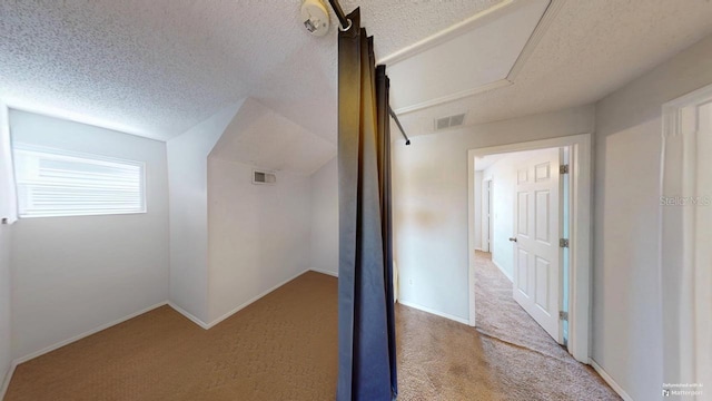 corridor featuring visible vents, carpet floors, a textured ceiling, and vaulted ceiling