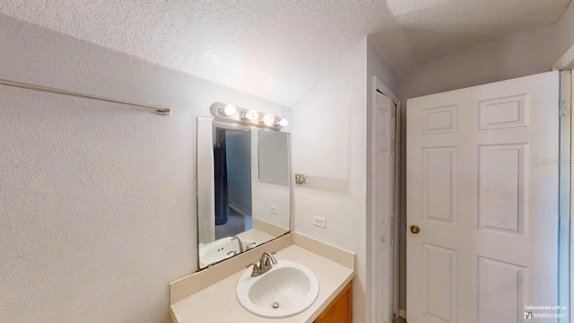 bathroom with a textured ceiling, vanity, and a textured wall