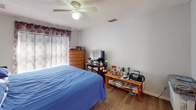 bedroom featuring a ceiling fan, wood finished floors, visible vents, and a textured ceiling