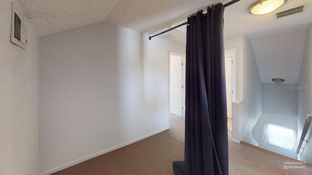 hallway with visible vents, a textured ceiling, wood finished floors, baseboards, and lofted ceiling