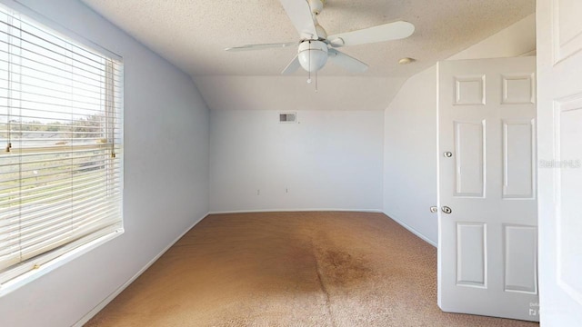 carpeted empty room featuring visible vents, baseboards, vaulted ceiling, a textured ceiling, and a ceiling fan