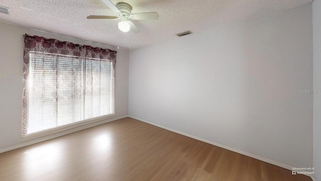 empty room featuring baseboards, wood finished floors, visible vents, and a textured ceiling