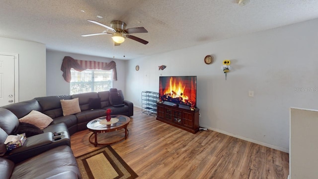 living area with baseboards, a textured ceiling, a ceiling fan, and wood finished floors