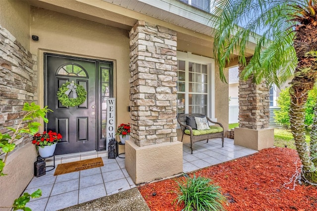 entrance to property featuring stone siding, stucco siding, and a porch