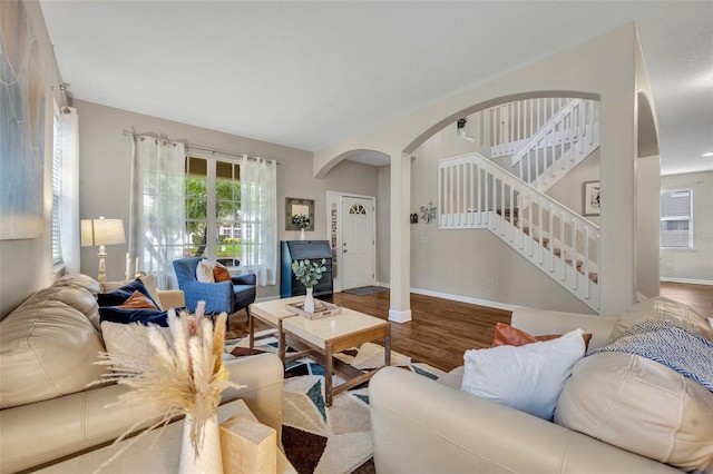 living area featuring stairs, wood finished floors, arched walkways, and baseboards