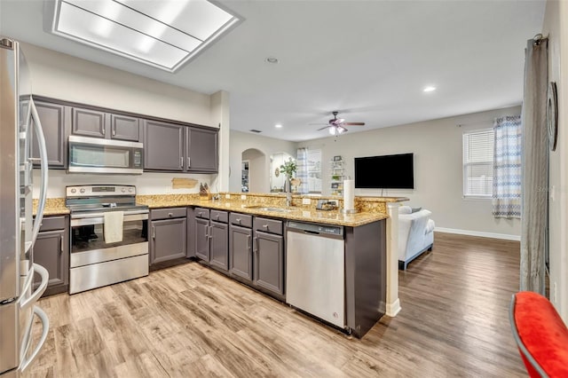 kitchen featuring arched walkways, a sink, gray cabinetry, appliances with stainless steel finishes, and open floor plan