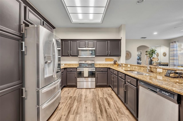 kitchen with light stone counters, arched walkways, a sink, appliances with stainless steel finishes, and light wood-type flooring