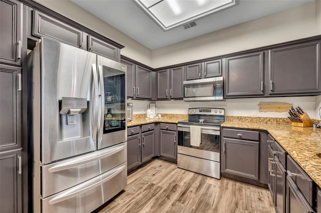 kitchen featuring light wood finished floors, light stone countertops, visible vents, and appliances with stainless steel finishes