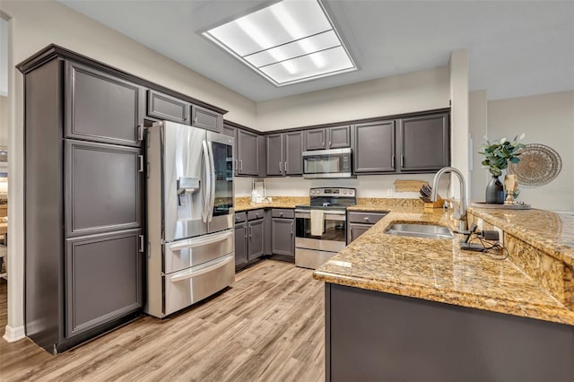 kitchen featuring a sink, light stone counters, light wood-style floors, appliances with stainless steel finishes, and a peninsula