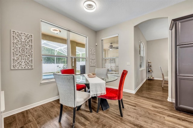 dining room with a textured ceiling, wood finished floors, arched walkways, and baseboards