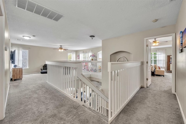 hallway with carpet, baseboards, visible vents, a textured ceiling, and an upstairs landing