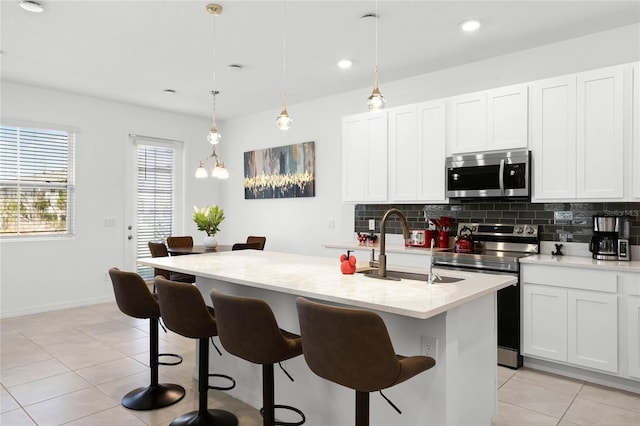 kitchen with tasteful backsplash, an island with sink, light tile patterned floors, a kitchen breakfast bar, and stainless steel appliances