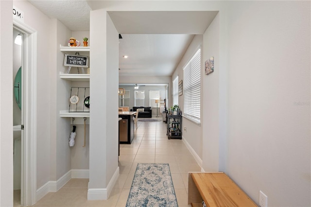 corridor featuring light tile patterned floors, built in shelves, and baseboards