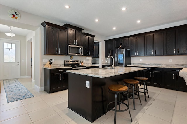 kitchen featuring light stone counters, light tile patterned floors, a breakfast bar, a sink, and stainless steel appliances