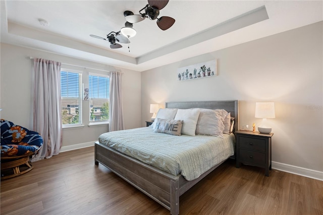 bedroom featuring baseboards, a raised ceiling, and wood finished floors