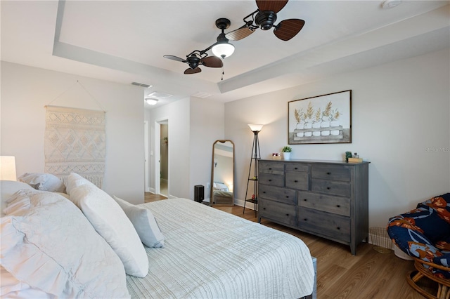 bedroom with ceiling fan, a tray ceiling, visible vents, and wood finished floors