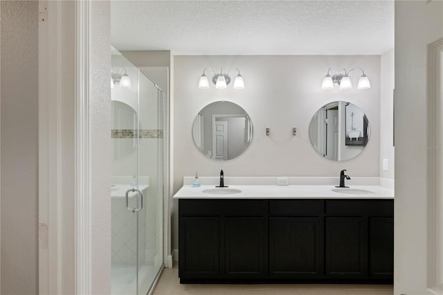 full bathroom with a textured ceiling, double vanity, a stall shower, and a sink