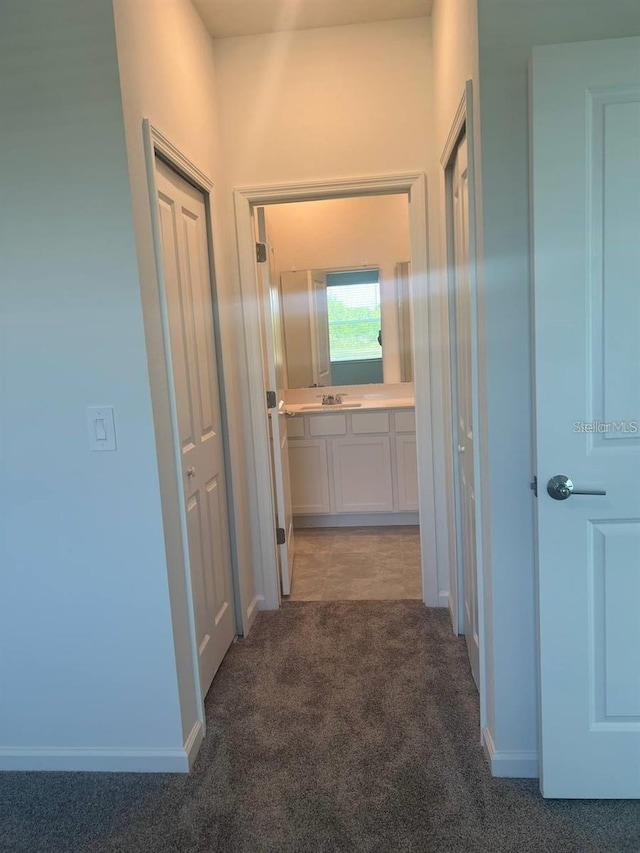 hall featuring baseboards, carpet floors, and a sink