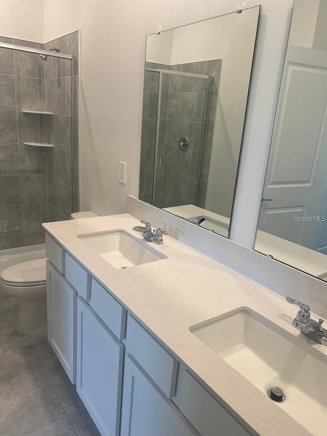 bathroom with a tile shower, double vanity, toilet, and a sink