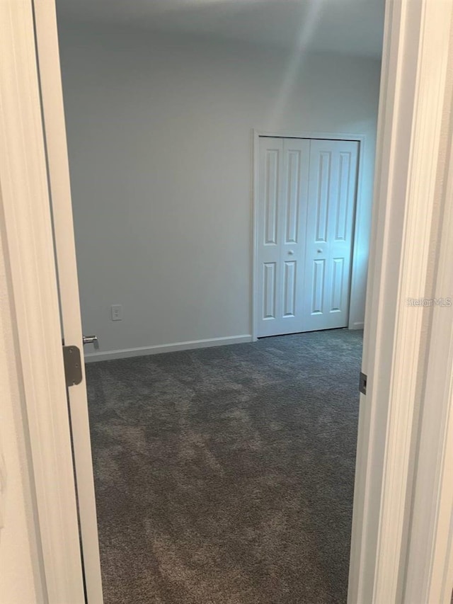 unfurnished room with dark carpet and baseboards