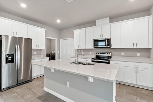 kitchen with a kitchen island with sink, a sink, appliances with stainless steel finishes, white cabinets, and light countertops