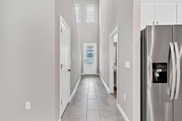 doorway to outside with light tile patterned floors, baseboards, a healthy amount of sunlight, and a towering ceiling