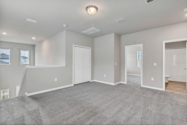 unfurnished bedroom featuring a textured ceiling, carpet, visible vents, and baseboards