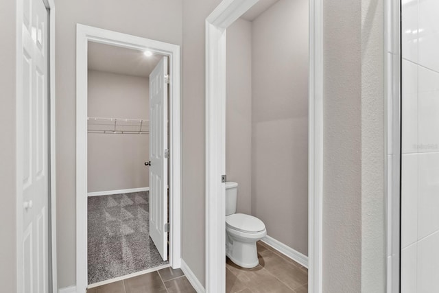 bathroom featuring a spacious closet, toilet, and baseboards
