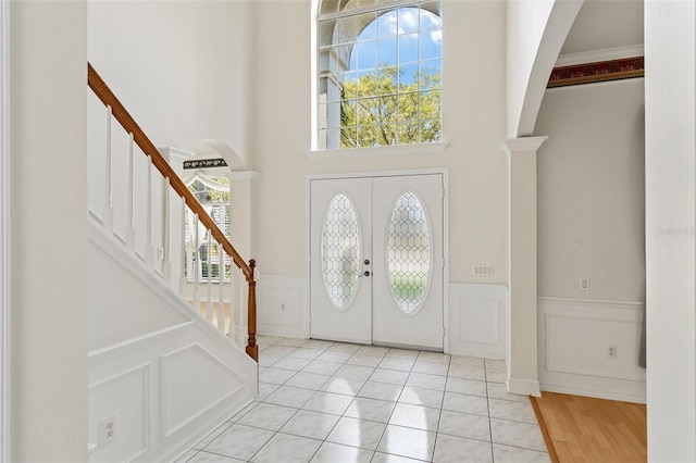 entryway with stairs, a decorative wall, french doors, and wainscoting