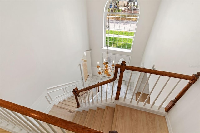 stairway featuring a decorative wall, an inviting chandelier, and wood finished floors