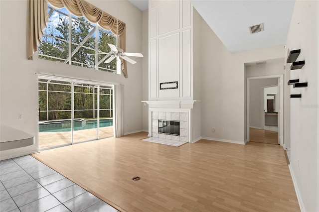 unfurnished living room with visible vents, light wood-style flooring, a ceiling fan, a fireplace, and a towering ceiling