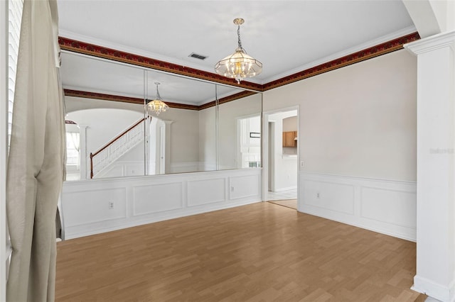 unfurnished room featuring visible vents, ornamental molding, wood finished floors, arched walkways, and a decorative wall