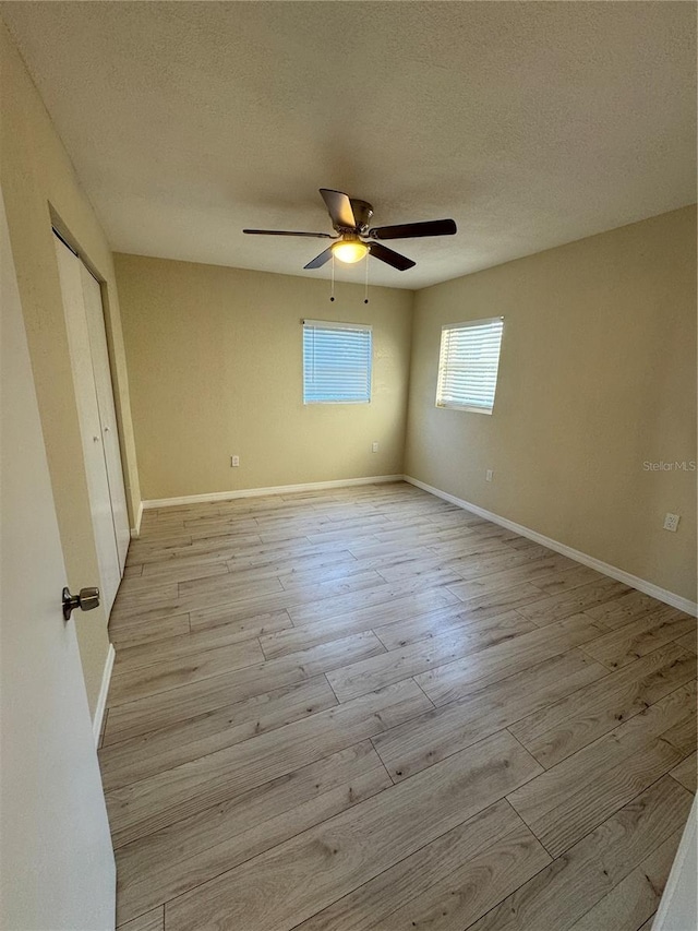 unfurnished bedroom featuring baseboards, a textured ceiling, and light wood-style flooring