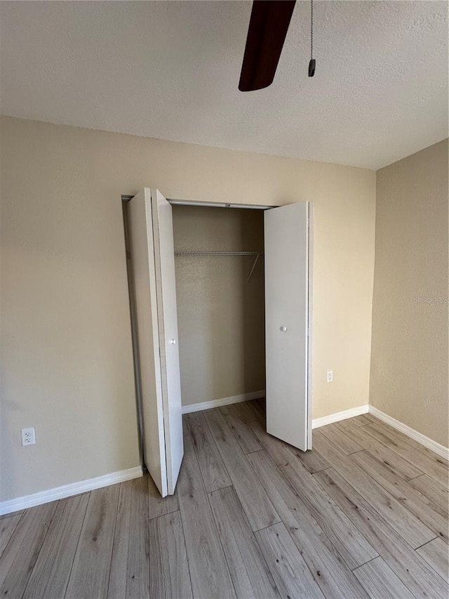 unfurnished bedroom featuring a textured ceiling, wood finished floors, a closet, and baseboards