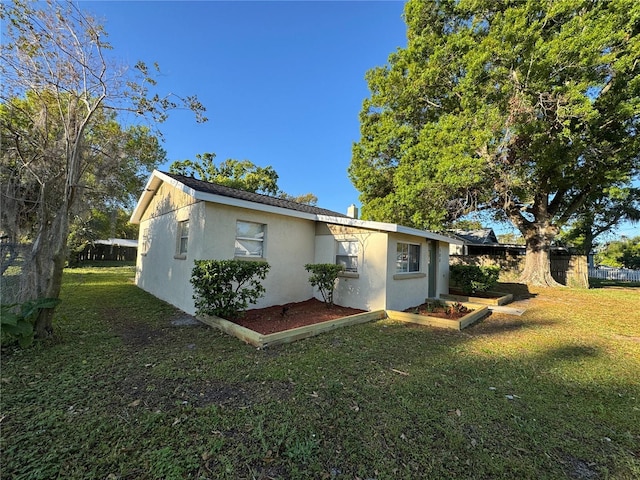 rear view of house featuring stucco siding, a yard, and fence