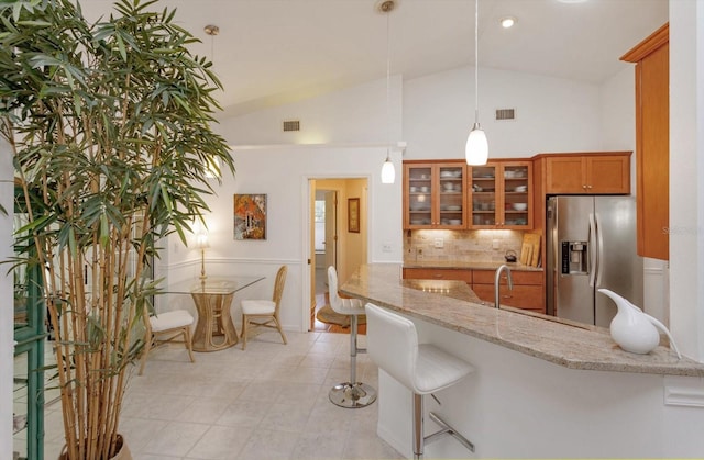 kitchen with stainless steel fridge, brown cabinets, vaulted ceiling, and visible vents