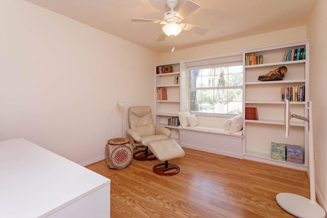 living area featuring a ceiling fan, baseboards, and wood finished floors