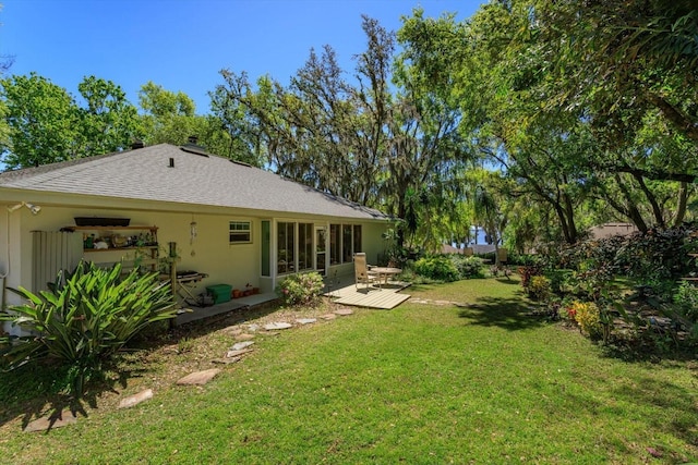 back of property featuring stucco siding, roof with shingles, a wooden deck, and a yard