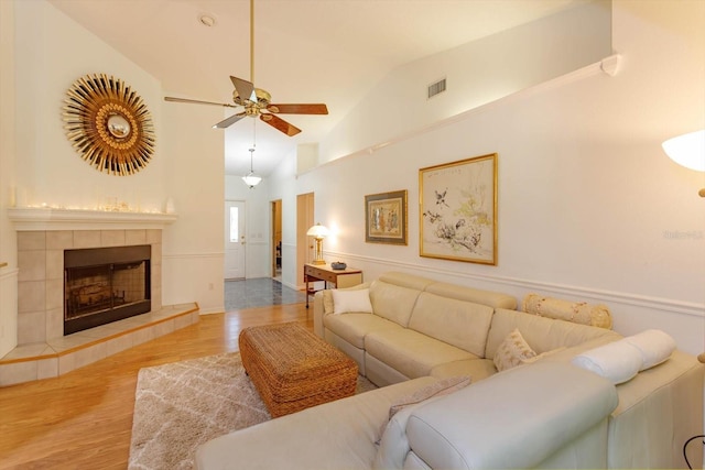 living area with ceiling fan, visible vents, a tiled fireplace, wood finished floors, and vaulted ceiling