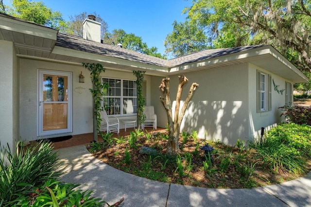 entrance to property featuring a porch, a shingled roof, stucco siding, and a chimney
