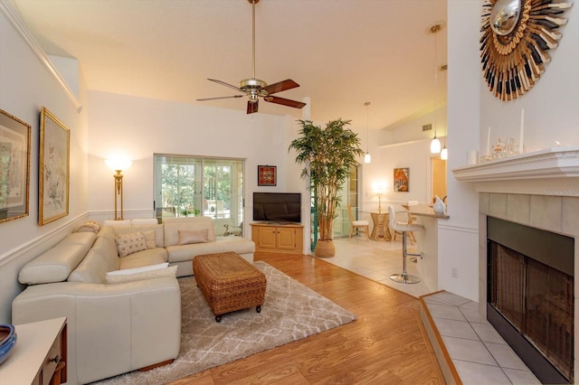 living area featuring a tiled fireplace, a high ceiling, a ceiling fan, and wood finished floors