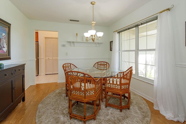 dining area featuring visible vents, light wood finished floors, baseboards, and a notable chandelier