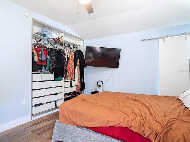 bedroom featuring vaulted ceiling, a barn door, wood finished floors, and ceiling fan