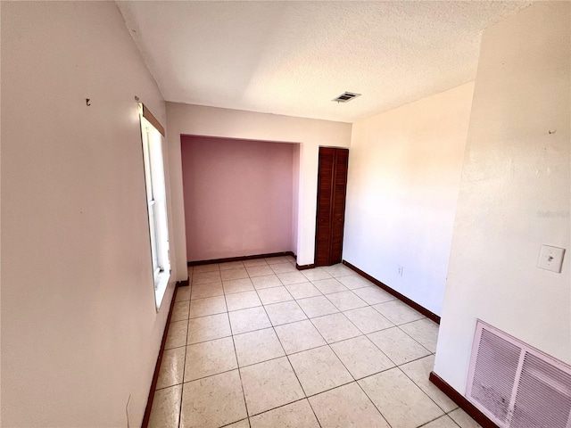 unfurnished room featuring light tile patterned floors, baseboards, visible vents, and a textured ceiling