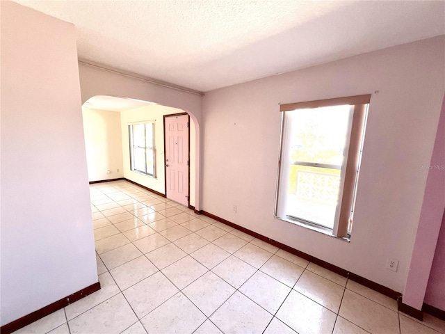 empty room with light tile patterned floors, baseboards, arched walkways, and a textured ceiling