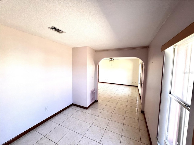 empty room with baseboards, visible vents, light tile patterned flooring, arched walkways, and a textured ceiling